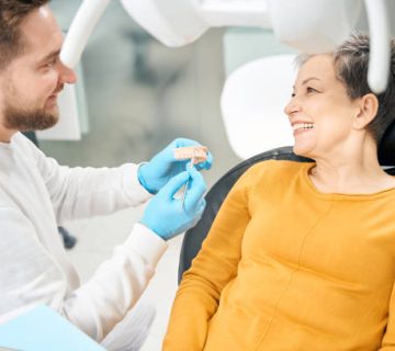cheerful aesthetic dentist showing to client how he treat her tooth