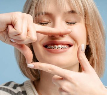 cheerful caucasian young woman patient with braces making frame from hands showing teeth with 1