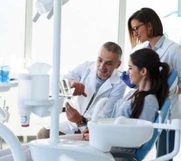 dentist and his assistant in dental office talking with young female patient and preparing
