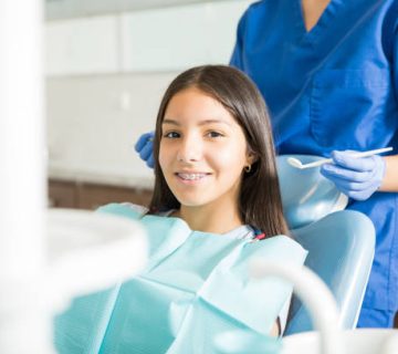 dentist standing behind smiling teenage girl with braces in clinic 2