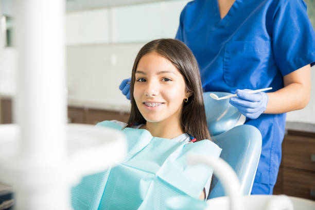 dentist standing behind smiling teenage girl with braces in clinic 2