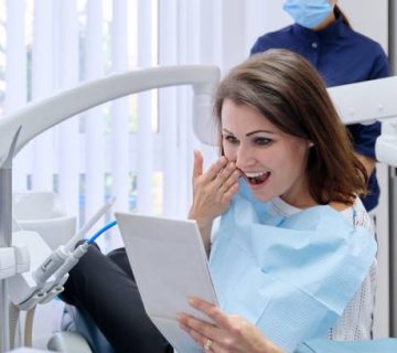 happy middle aged woman with doctor dentist looking in mirror at teeth 1