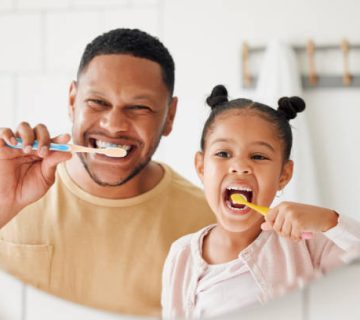 happy mixed race father and daughter brushing their teeth together in a bathroom at home 2