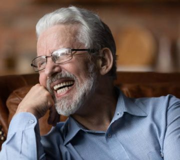 mature man sit on sofa laugh demonstrate healthy straight teeth