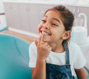 mixed race little patient showing her perfect toothy smile while sitting dentists chair 1