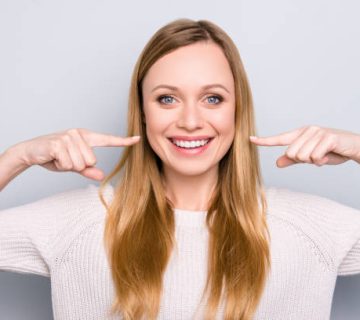 portrait of joyful satisfied girl gesturing her beaming white healthy teeth with two