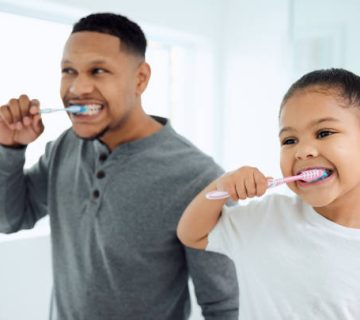 shot of an adorable little girl and her father brushing their teeth together at home