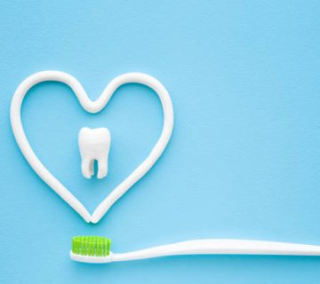 toothbrush with green bristles on pastel blue background heart shape created from paste white