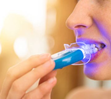 woman is whitening teeth with special toothpaste and led light at home beauty concept