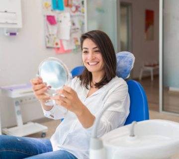young woman looking at mirror with smile in dentists office